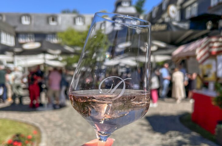 Hände halten ein Weinglas mit Deimann-Logo gefüllt mit Rosé auf dem Sommerfest