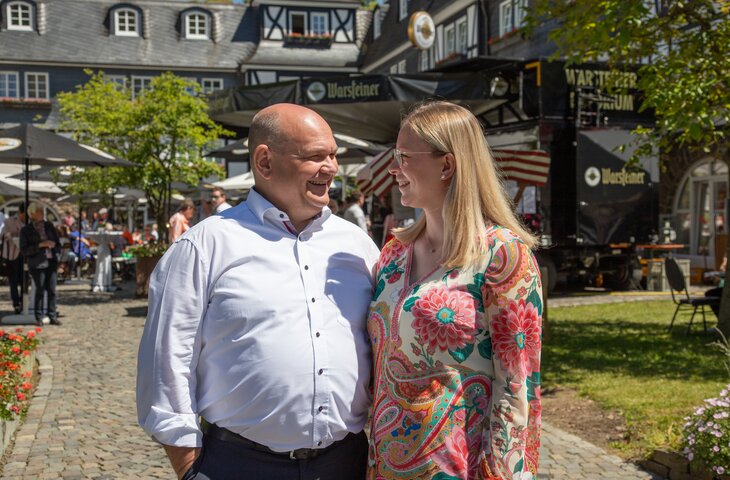 Ein Mann und eine Frau lächeln sich an, im Hintergrund das Sommerfest des Hotel Deimann